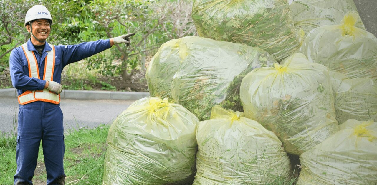ゴミの山を指さす草刈りの職人